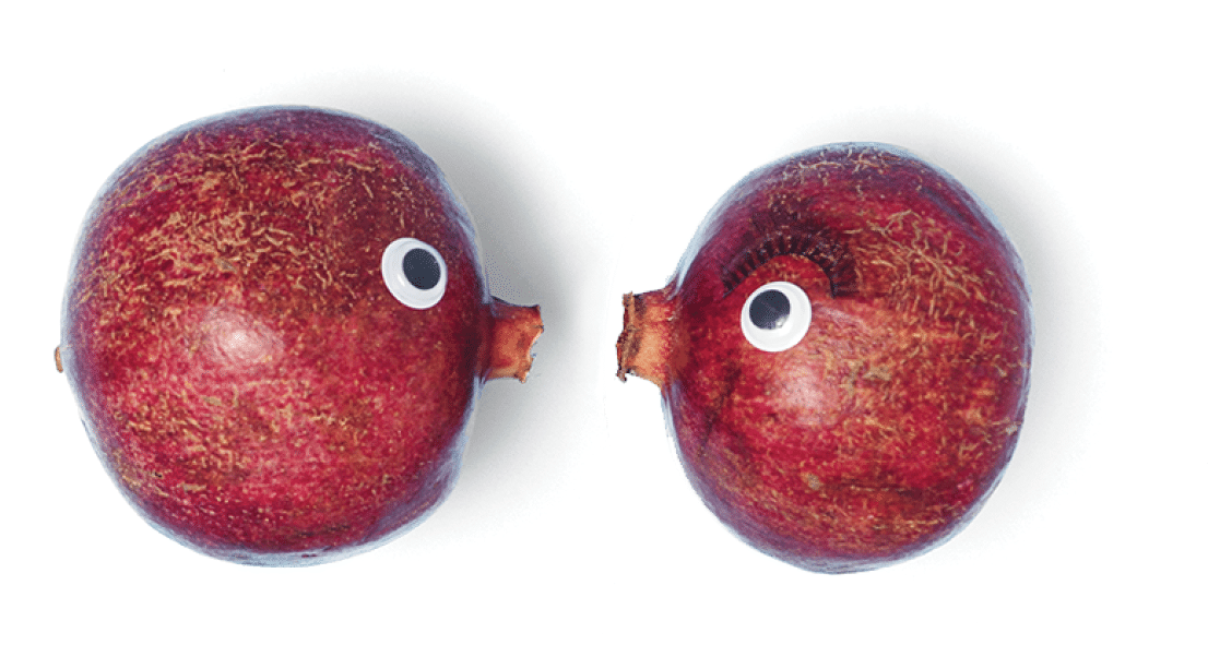 Flat lay arrangement consist of two pomegranates with pomegranate seeds form heart shape on the pastel blue background  Used wiggle googly eyes and false eyelashes 